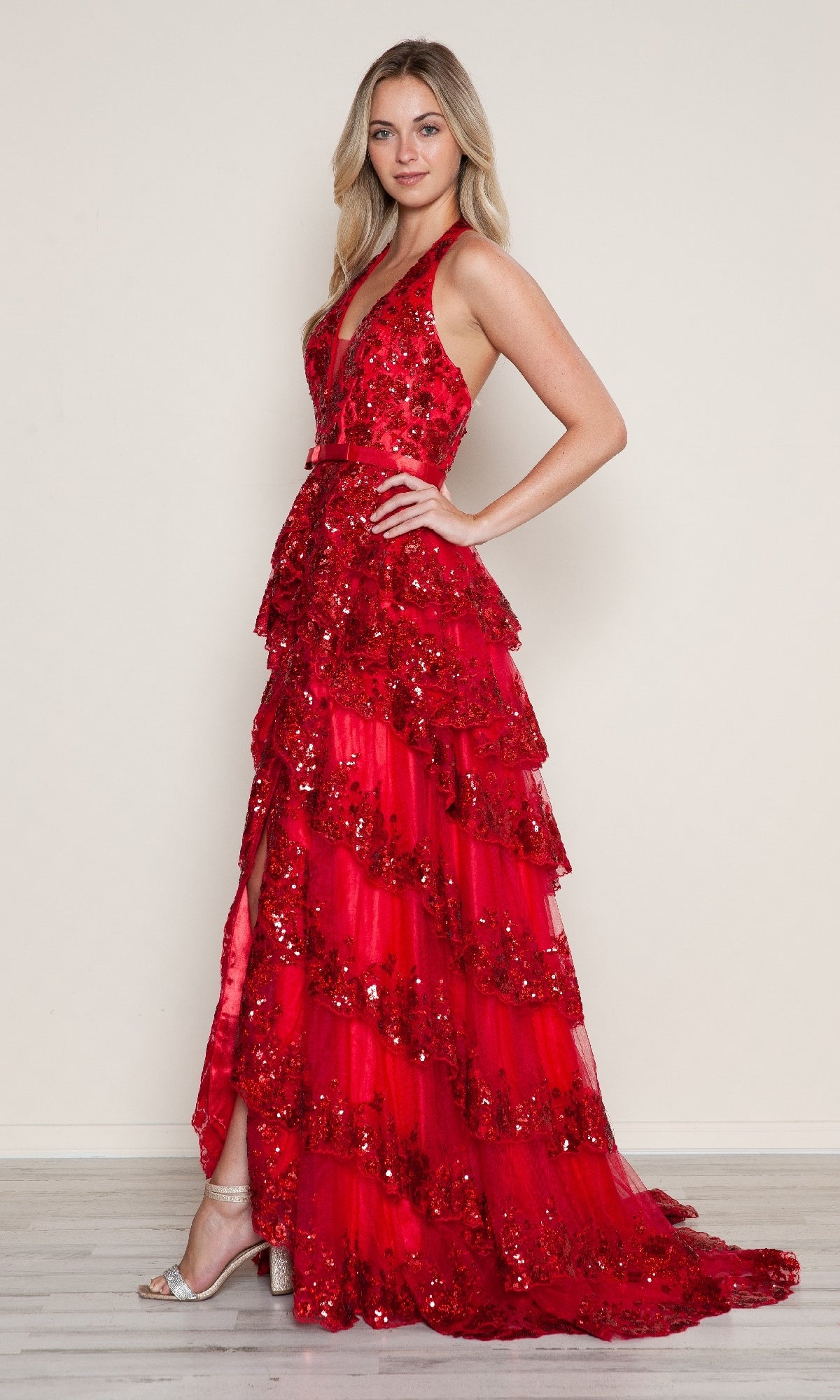 A woman stands against a plain light background in the Poly USA 9618, a sleeveless, floor-length sequin prom dress with tiered ruffles, paired with silver high-heeled sandals.